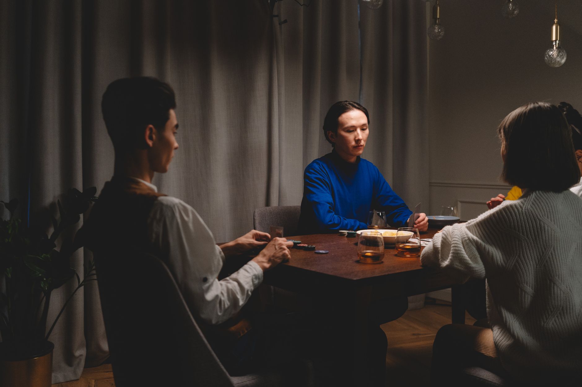 Capture an intimate group enjoying a poker game with whiskey glasses, indoors.