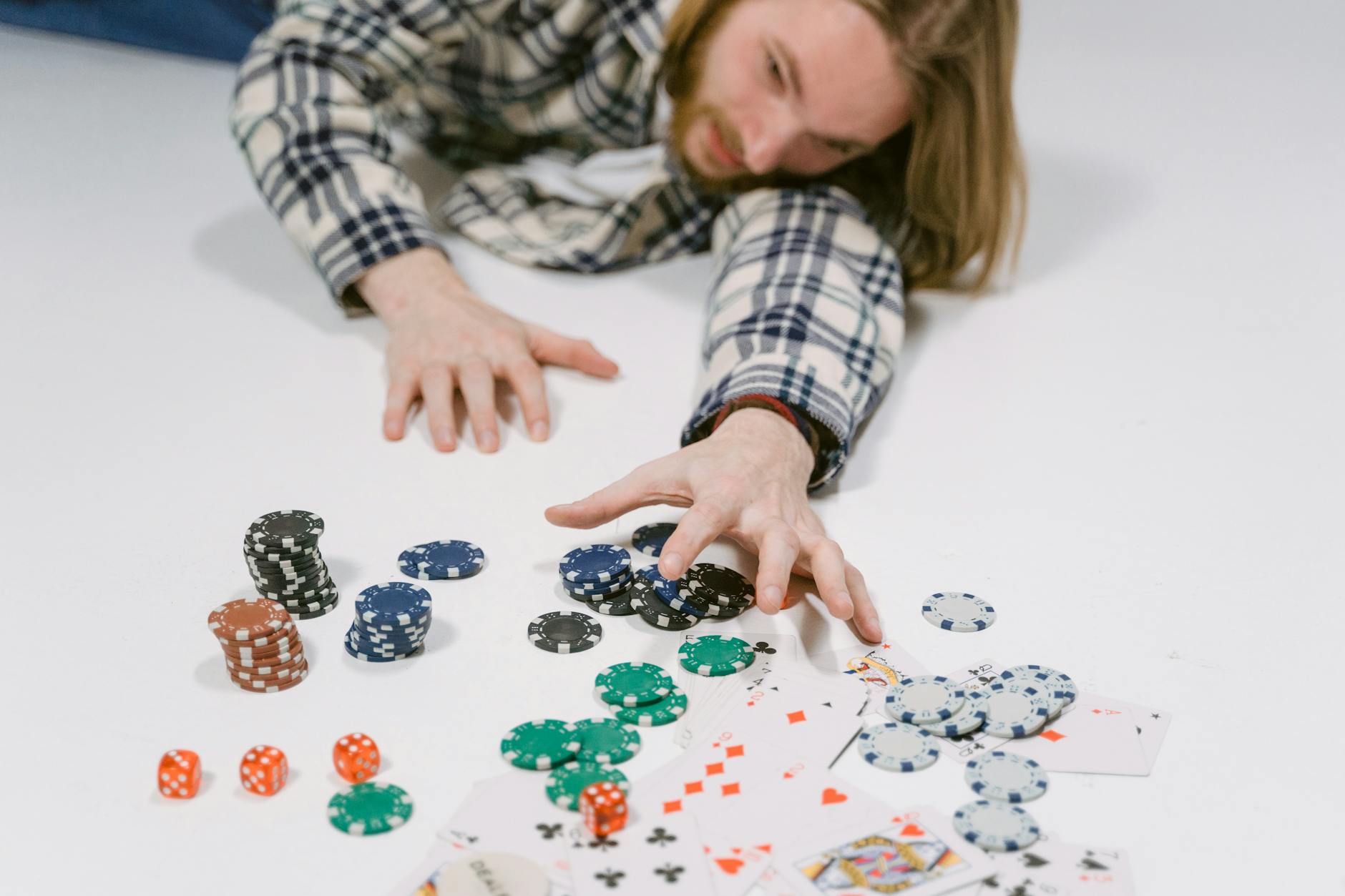 A man in a plaid shirt reaches for poker chips on a white surface, depicting a gambling scene.