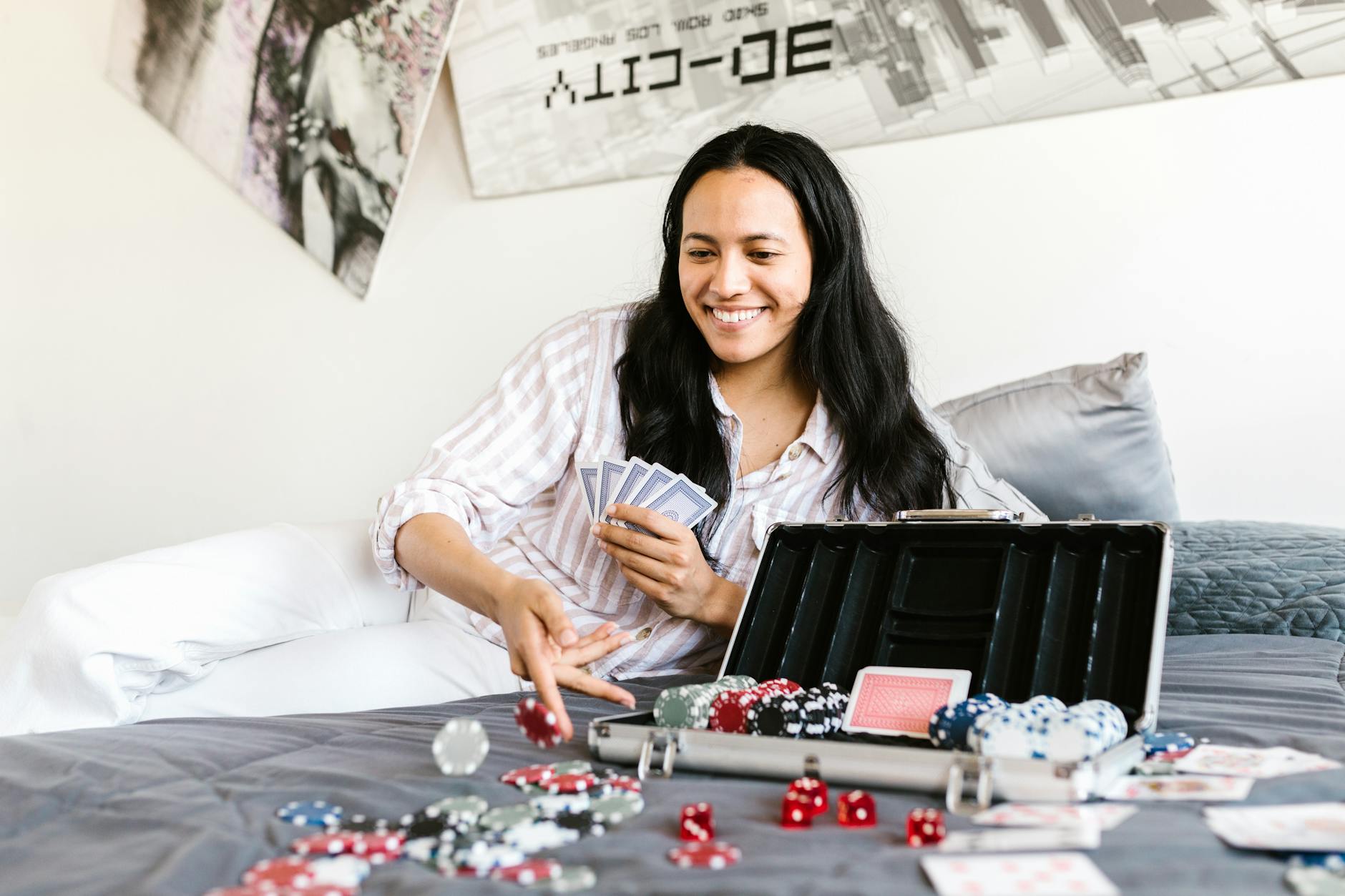 Smiling woman enjoying a game of poker with cards and chips on a bed.
